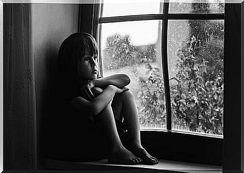 Sad child sitting in a window to represent children with low self-esteem